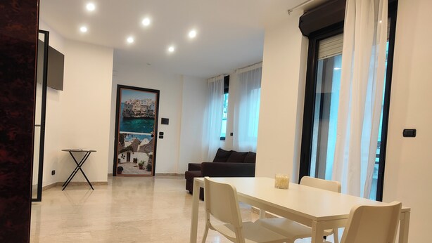 A modern living room with a dining area, a sofa, and a TV mounted on the wall. - CconfortHotels eXtramurale Apartment (Bari)