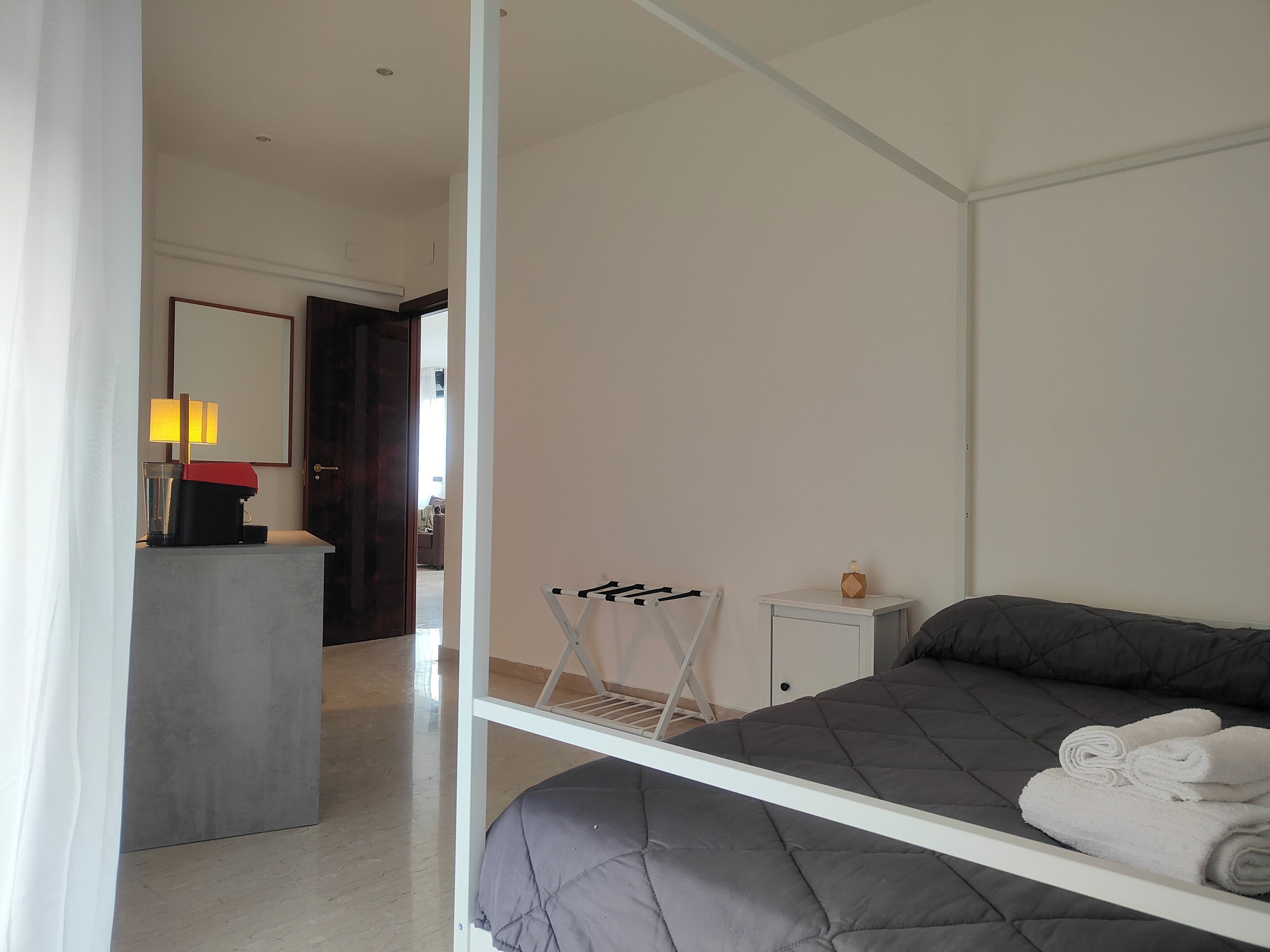 A hotel room with a bed, a small bedside table, a lamp, and a view of the hallway.