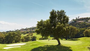 A golf course with a prominent tree in the foreground, a clear sky, and distant buildings on a hill. - T1 with exceptional sea view-HAMEAU CAP ESTEREL- VILLAGE VACANCES -AGAY (Saint-Raphaël)