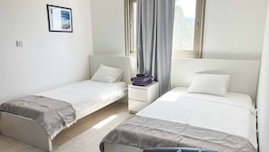Une chambre avec deux lits simples, une petite table de chevet, une chaise et une fenêtre avec des rideaux.