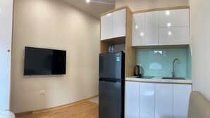 Una kitchenette compacta con refrigerador, pileta y televisor de pantalla plana montado en la pared.