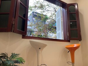Una habitación con ventana, una lámpara de pie blanca y una lámpara cónica naranja.