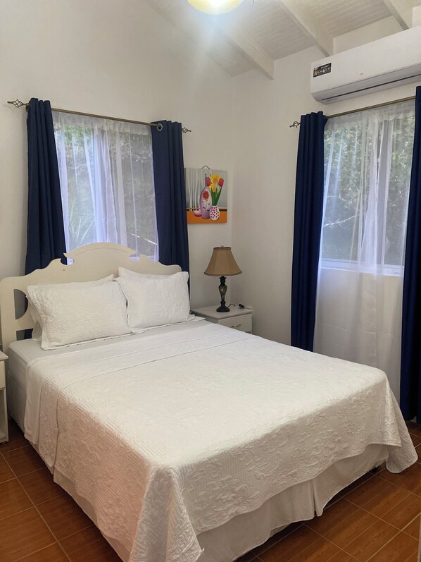 A neatly made bed with white linens, a bedside lamp, and a nightstand. - 1-bedroom condo in charming Choiseul with AC, WiFi. Book now (Castries)