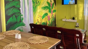 Uma área de refeições com uma mesa, cadeiras, uma TV na parede e um mural com uma cascata e selva.