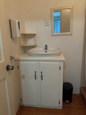 A bathroom with a white sink, a mirror, and a trash bin. - 1-bedroom condo in charming Choiseul with AC, WiFi. Book now (Castries)