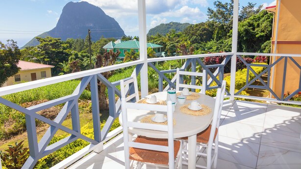 Uma área de estar coberta ao ar livre, com uma mesa posta para dois, com vista para um jardim exuberante e uma montanha.