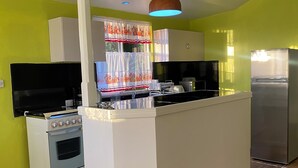 Uma cozinha com ilha central, armários brancos, forno embutido, geladeira e televisão.