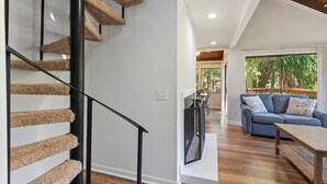 A modern interior with a spiral staircase, a living area with a sofa and coffee table, and a dining area with chairs and a TV.