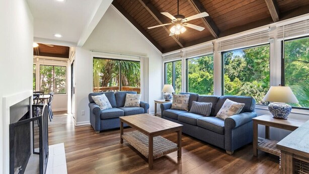A spacious living room with a high ceiling, large windows, and a ceiling fan.