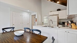 A modern kitchen with white cabinets, a wooden dining table, and a built-in microwave.