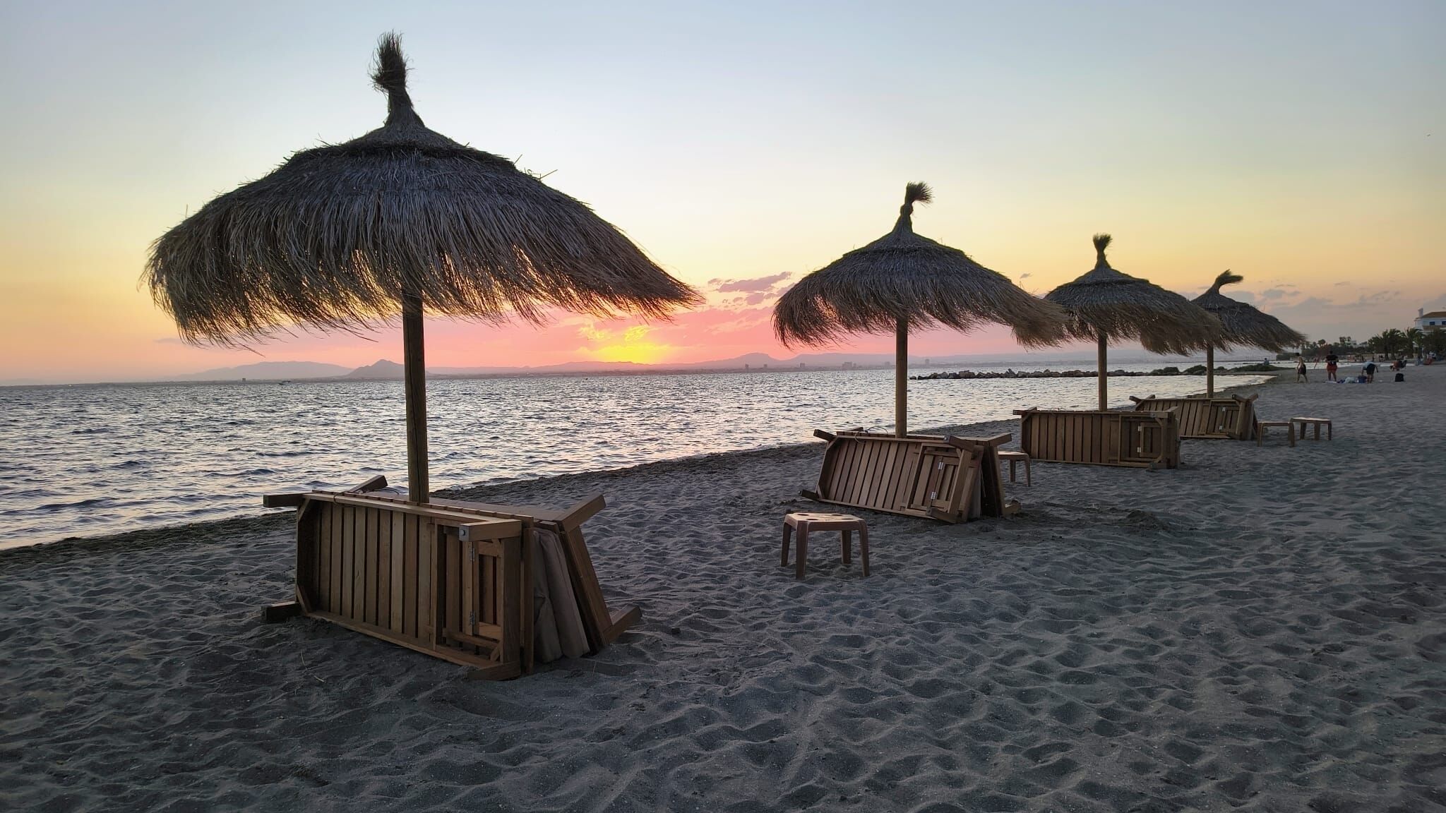 Una spiaggia con ombrelloni di paglia e sedute in legno.