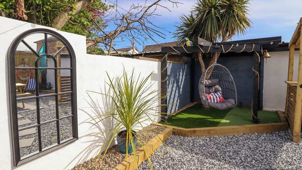 A cozy backyard with a hanging chair, a small garden, and a wooden deck.