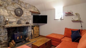 A cozy living room with a stone fireplace, orange sofas, a flat-screen TV, and a wooden coffee table.