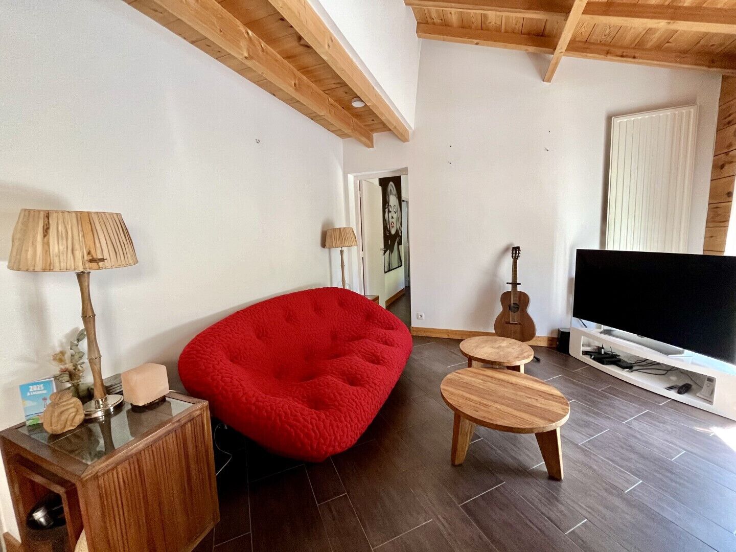 A living room with a red bean bag chair, a small wooden table, a television, and a guitar.