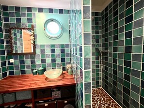 A bathroom with a wooden vanity, a round mirror, and a shower area with green and black tiles. - Villa Maryline by Agence Bru - 548080 (Lacanau)