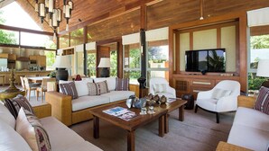 Un salón amplio con techo de madera, ventanas grandes, televisor y asientos cómodos.