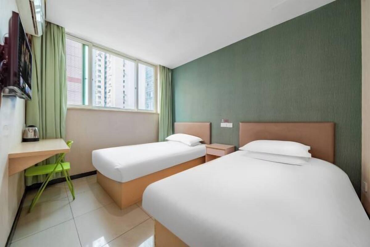 A hotel room with two beds, a desk, a chair, and a window with a view of buildings.
