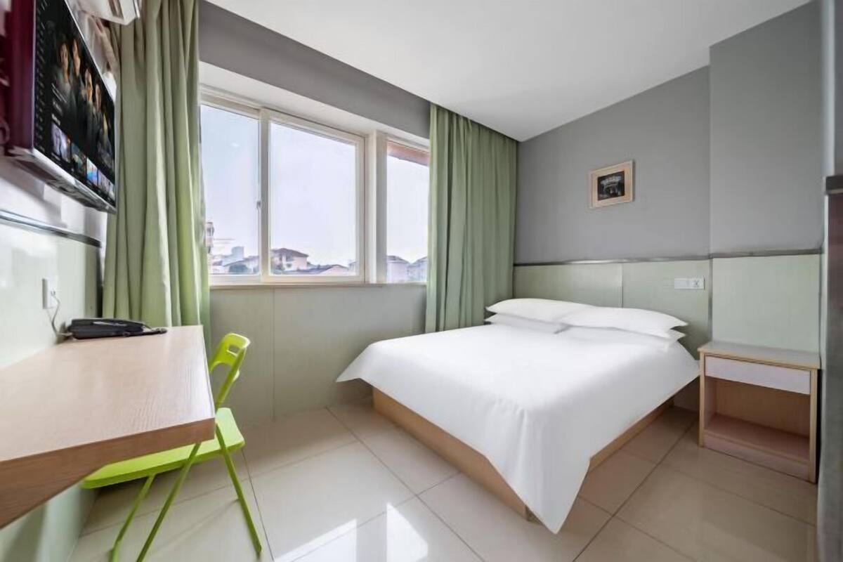 A hotel room with a bed, a desk, a chair, a TV, and a window with curtains.