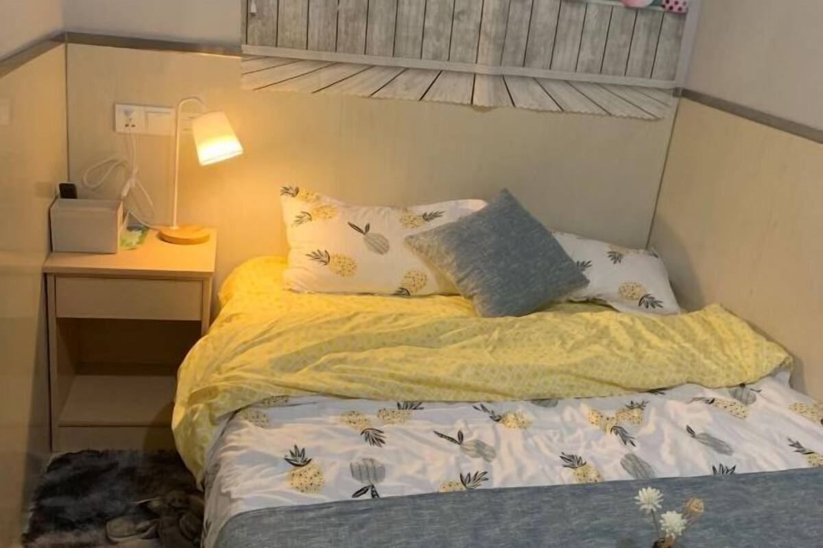 A bedroom with a bed, a nightstand, a lamp, and a wall-mounted shelf.