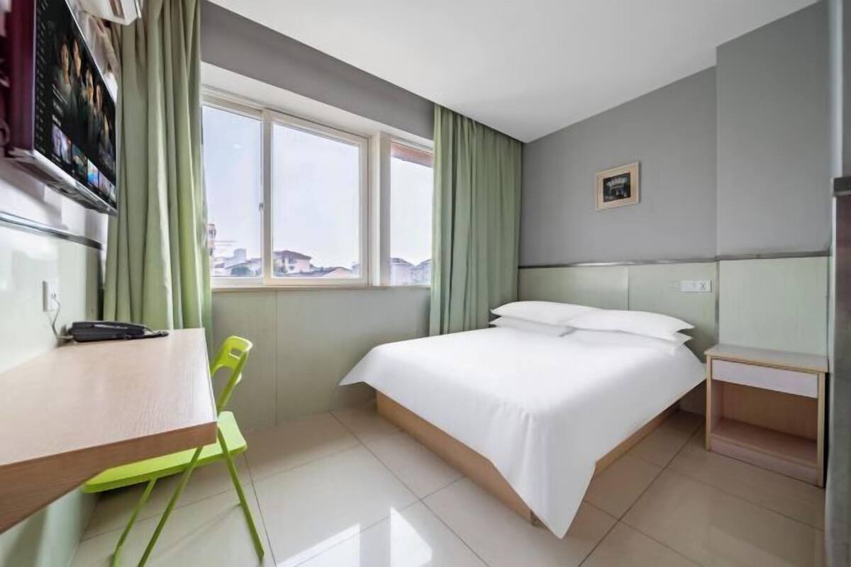 A hotel room with a bed, a desk, a chair, a window, and a television.