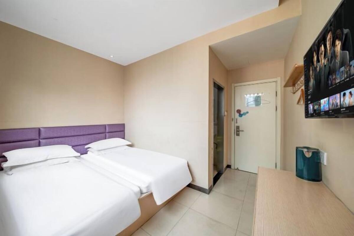 A hotel room with two beds, a wooden desk, a television mounted on the wall, and a door leading to another room.