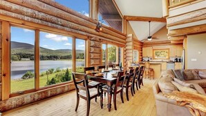 Una cabana de fusta amb menjador, cuina i un gran finestral amb vista a un llac.