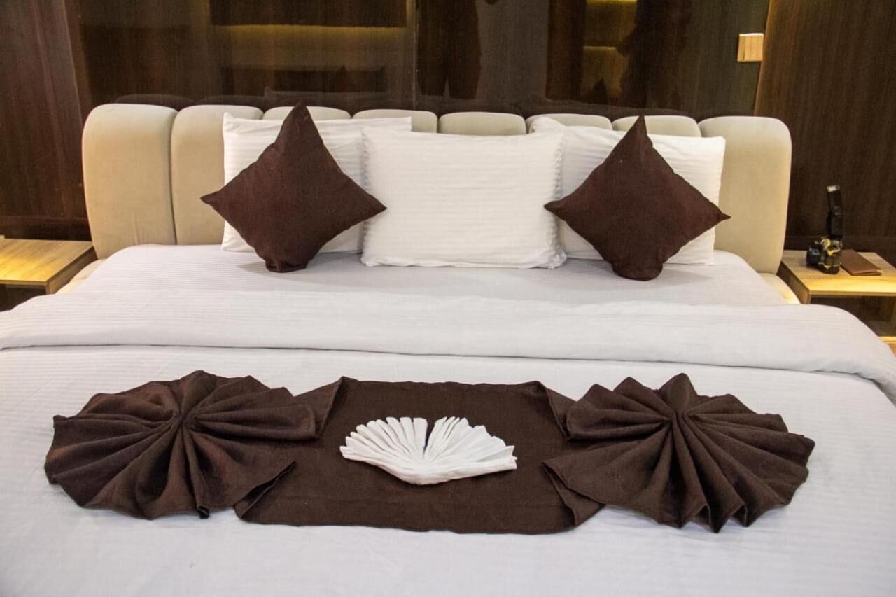 Hotelkamer met een groot bed, twee bruine kussens, een wit kussen en een decoratieve bruine stof op het bed.