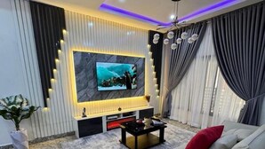 Un salon moderne avec un grand téléviseur à écran plat fixé au mur, un canapé beige, une table basse et une plante en pot.