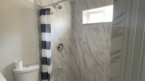 Ein Badezimmer mit Toilette, Dusche und einer Wand mit Marmorfliesen.