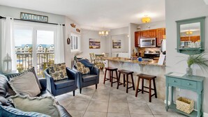 A modern living room with a sofa set, a dining area, and a kitchen with wooden cabinets. - Beachfront  - Fantastic Beach Vacation for Family Fun (Gulf Shores)