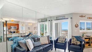 A modern living room with a dark blue sofa, two armchairs, and a mirrored wall reflecting the kitchen area. - Beachfront  - Fantastic Beach Vacation for Family Fun (Gulf Shores)