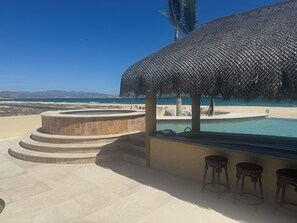 A pool area with a thatched roof, a hot tub, and a view of the beach and mountains. - Ocean Front Villa in peaceful La Ribera Sleeps 8 (La Ribera)