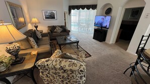 A living room with a sofa, armchairs, a coffee table, a TV, and a lamp.