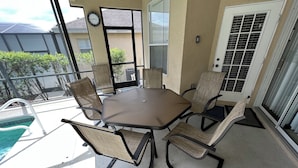 A patio with a table and chairs, a pool, and a view of neighboring houses.