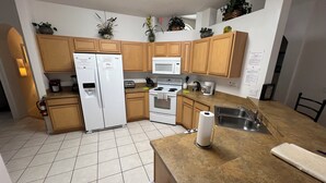 A kitchen with wooden cabinets, a refrigerator, a microwave, a stove, a sink, and various kitchen appliances.