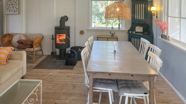 En hyggelig stue med pejs, spisebord og et vindue med udsigt til grønne omgivelser.