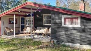 En hyggelig hytte med veranda, fletmøbler og et vindue med gardiner.