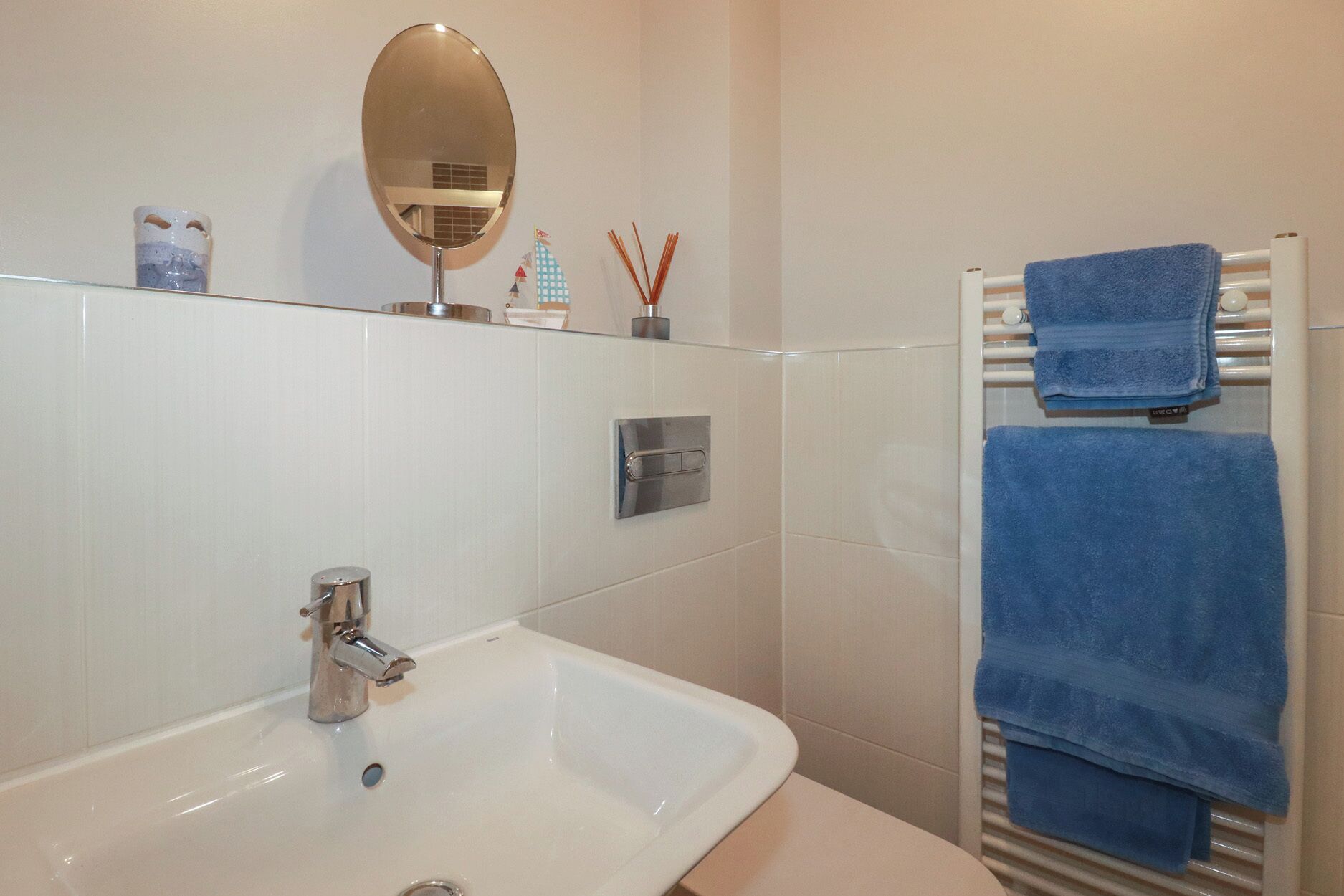 A bathroom with a white sink, a mirror, a towel rack with blue towels, and a small decorative item on the wall.