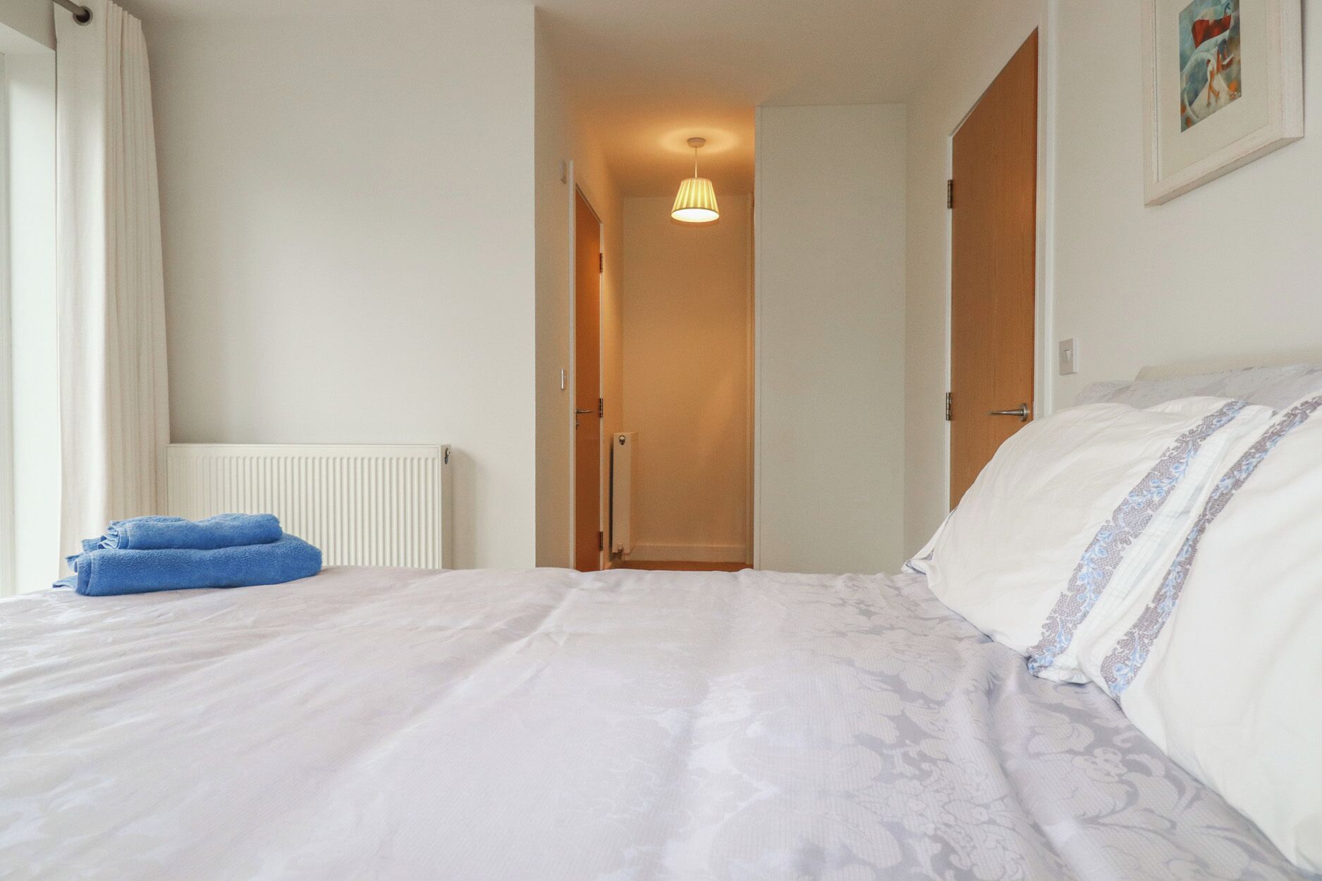 Une chambre d’hôtel avec un lit, un radiateur, une porte et un couloir menant à une autre pièce.