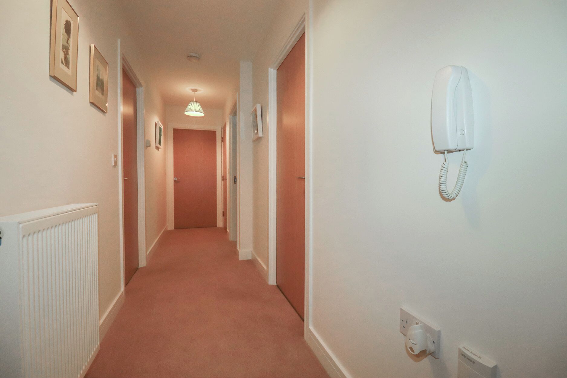 A hallway with a radiator, a telephone, and framed pictures on the wall.