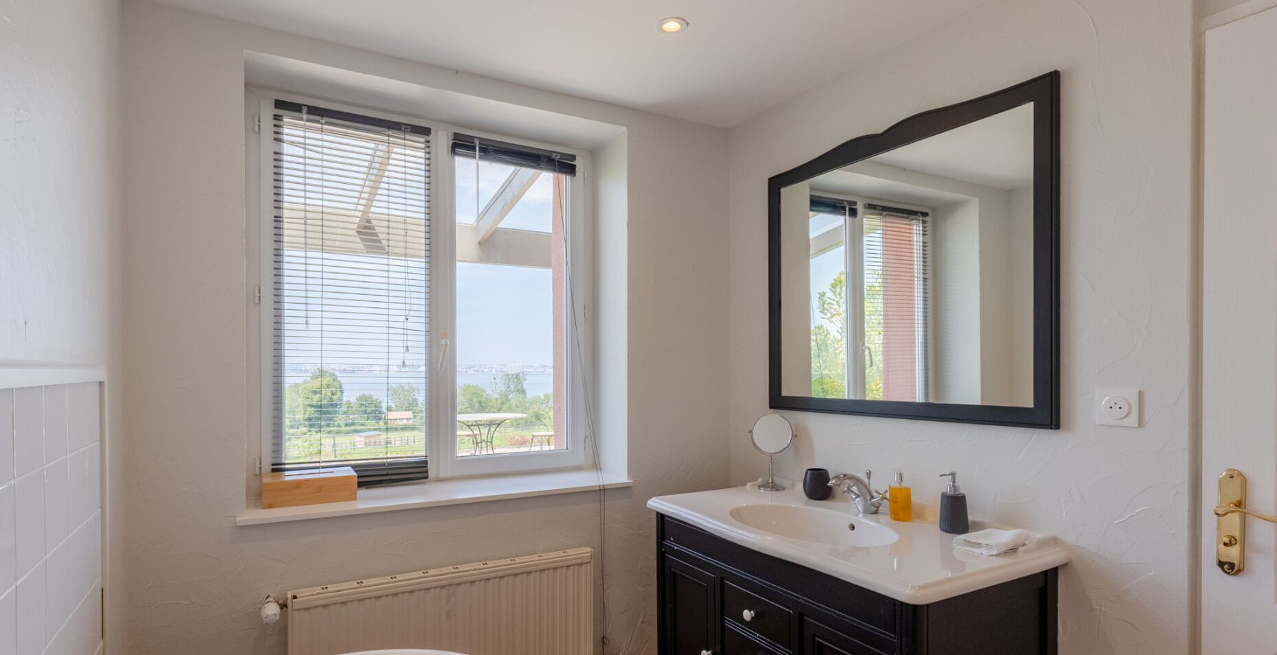 Un baño con ventana, lavamanos, espejo y radiador.