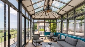 Une véranda dotée d’un toit en verre, aménagée avec un canapé, des fauteuils et une table basse.