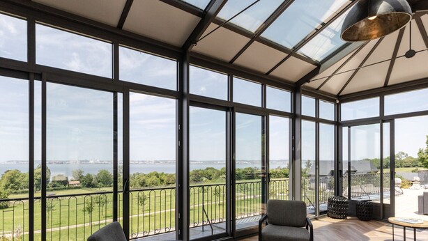 Une véranda dotée de grandes portes vitrées, donnant sur un parc, et aménagée avec du mobilier d’extérieur.