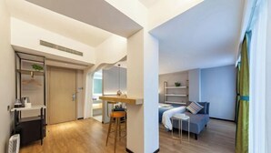 A modern hotel room with a kitchenette, a bed, a small table, and a sofa. - Allston Hotel (Xiamen)