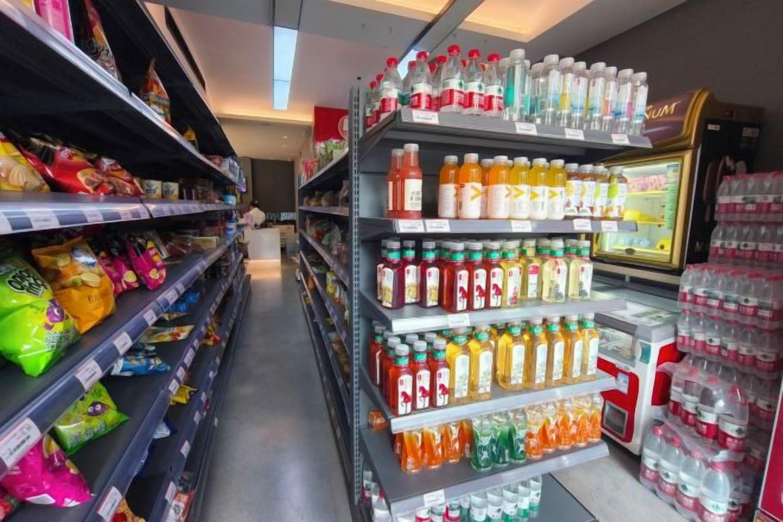 A grocery store aisle with shelves stocked with snacks, bottled beverages, and a refrigerated display.