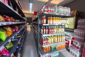 A grocery store aisle with shelves stocked with snacks, bottled beverages, and a refrigerated display. - Allston Hotel (Xiamen)