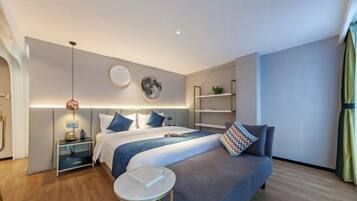 A modern hotel room with a large bed, bedside tables, a small round table, and a sofa.