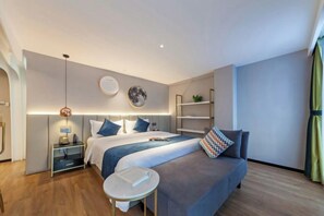 A modern hotel room with a large bed, bedside tables, a small round table, and a sofa. - Allston Hotel (Xiamen)