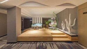 A modern lobby with a wooden reception desk, a light blue sofa, and a cactus sculpture. - Allston Hotel (Xiamen)