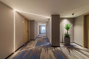 A hotel corridor with a carpeted floor, a potted plant, and a light fixture on the ceiling. - Allston Hotel (Xiamen)